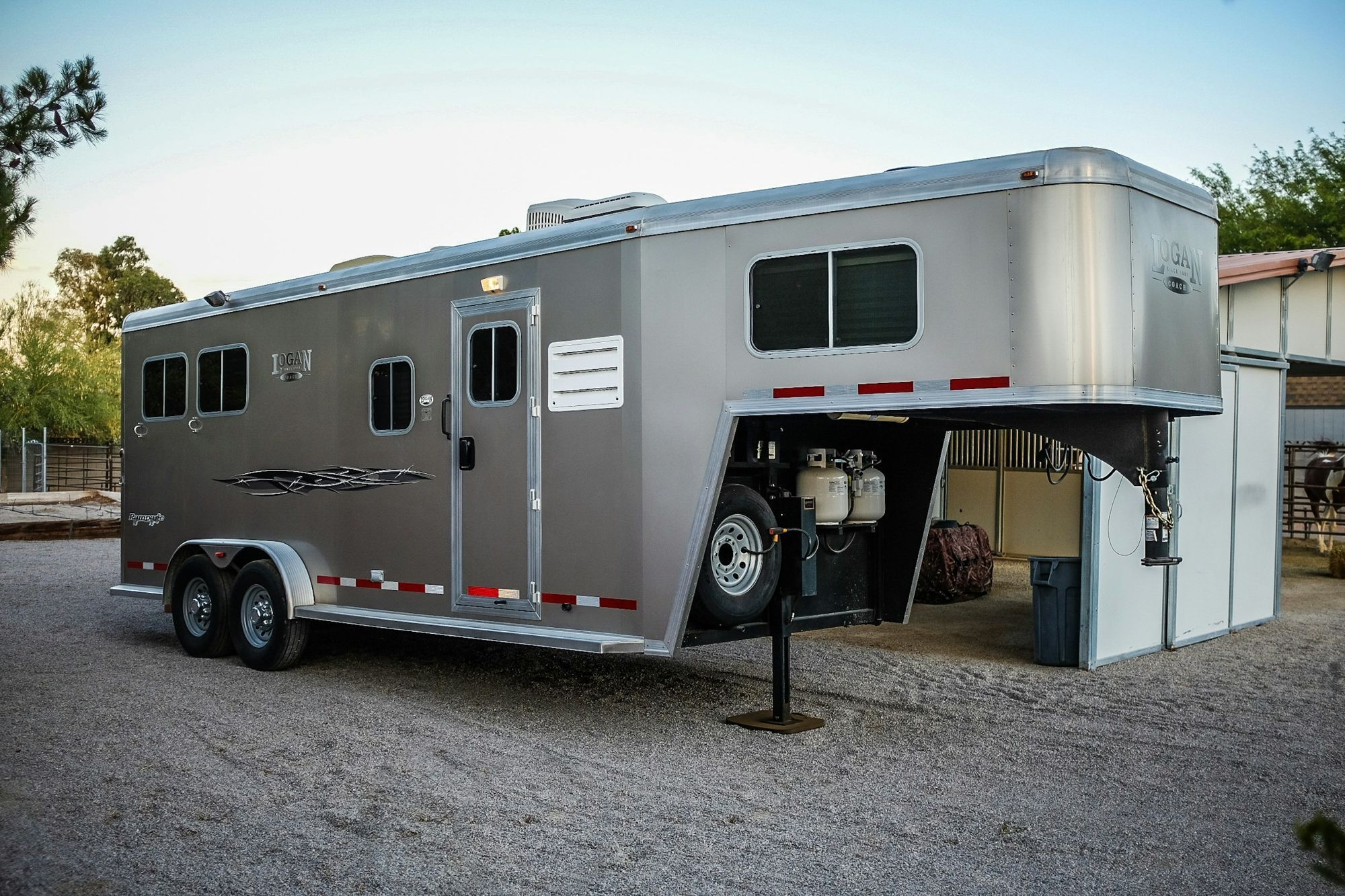 A gooseneck horse trailer with living quarters, parked at a barn