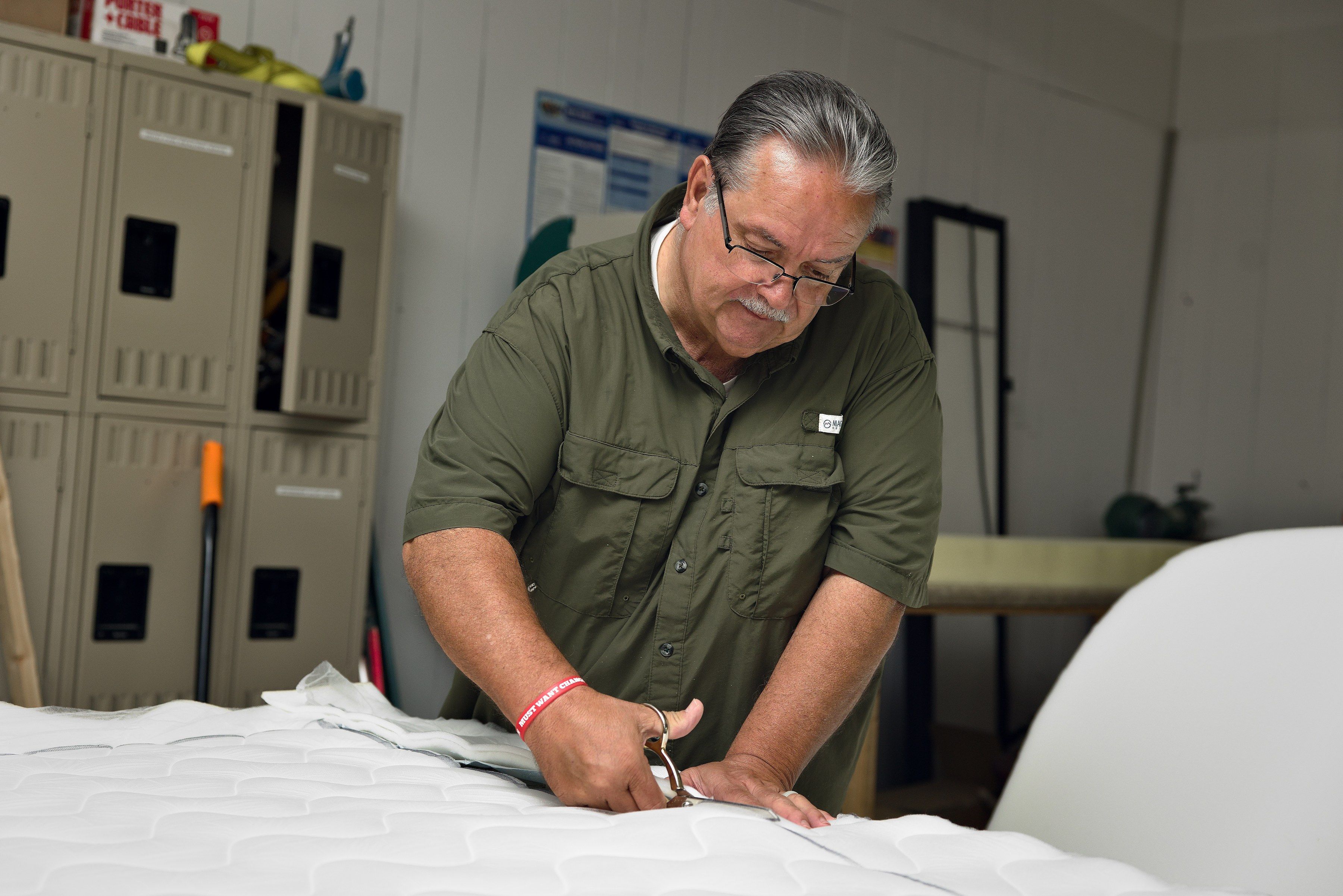 Clinton’s hands cutting white quilted ticking to size with shears on the shop table